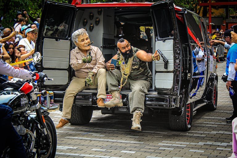 A vibrant street festival in Medellín featuring a classic van, costumed characters, and motorcycles.